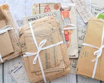 May include: A bundle of vintage sewing patterns wrapped in white ribbon. The patterns are for McCall's and include the numbers 4765 and 478. The patterns are in various shades of brown and beige.