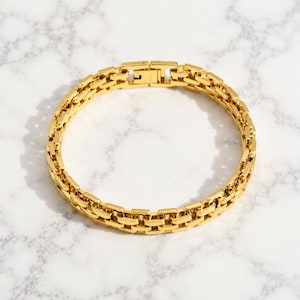 May include: A polished gold-tone bracelet featuring a series of interlocking rectangular links. The chain design creates a continuous circular band with a secure, integrated clasp mechanism visible at the top, showcasing a bright, reflective finish.