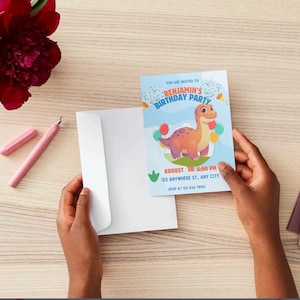 May include: A birthday party invitation featuring a cartoon dinosaur with balloons. The invitation is held in hands, with a white envelope, a pink pen, and a red flower in the background. The invitation reads "Benjamin's Birthday Party".