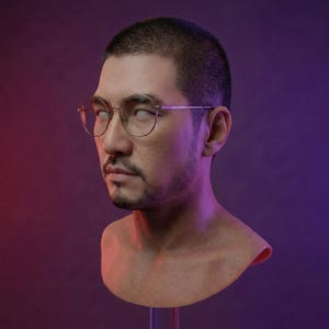 Op de afbeelding: Een buste van een persoon met kort donker haar en een getrimde baard, met een ronde, goudkleurige bril. De achtergrond loopt over van rood naar paars. De buste is op een transparante standaard gemonteerd.