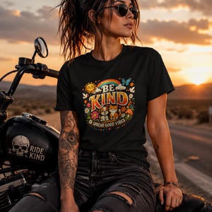 Peut inclure: Un t-shirt noir à manches courtes avec un imprimé graphique coloré représentant un arc-en-ciel, un soleil, des fleurs, un papillon, un chiot et un chaton. Le texte indique BE KIND et SPREAD GOOD VIBES dans une police audacieuse et rétro.