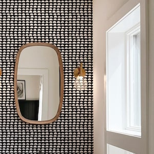May include: A bathroom vanity with a white countertop and wooden cabinets. The backsplash is a black and white geometric pattern. A large oval mirror hangs above the sink. The floor is white hexagonal tiles.