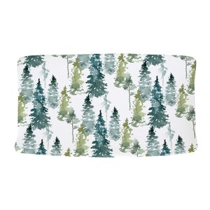 May include: A white fabric with a watercolor pattern of green and blue pine trees. The fabric has a subtle texture.