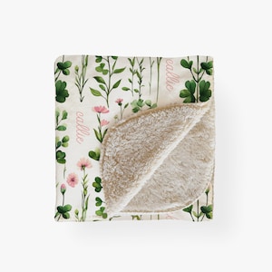 May include: A soft, white and cream colored fleece blanket with a floral pattern. The blanket has a green and pink floral design with the name "Callie" written in pink on both sides.