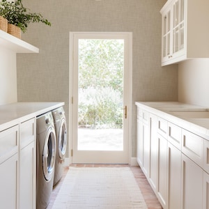 May include: A white laundry room with a white countertop, two stainless steel washing machines, and white cabinets. There is a door leading to the outside and a rug on the floor.
