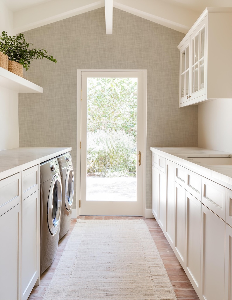 May include: A white laundry room with a white countertop, two stainless steel washing machines, and white cabinets. There is a door leading to the outside and a rug on the floor.