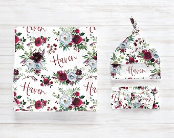 May include: A white baby blanket, hat, and headband set with a floral design. The pattern features burgundy, white, and blue flowers with green foliage. The name "Haven" is written in burgundy script on each item.