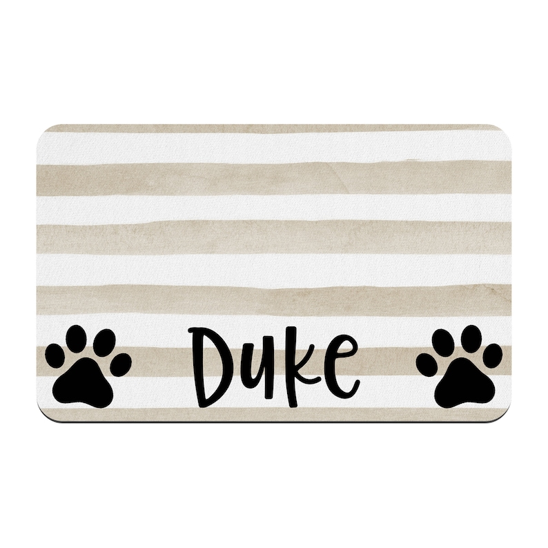 May include: Beige and white striped doormat with black paw prints on either side and the name "Duke" in black cursive lettering.