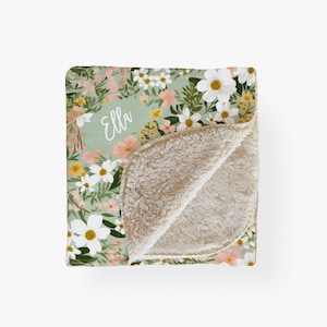 May include: A soft, green and white floral patterned blanket with a cream colored fleece lining. The blanket has the name "Ella" written in white on the front.