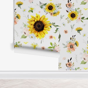 May include: A roll of wallpaper featuring a repeating pattern of watercolor sunflowers, small white daisies, and soft peach-colored blossoms on a light gray background. The design includes green foliage and stems scattered between the flowers.