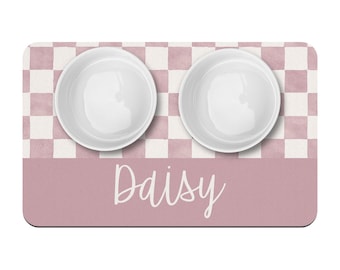 May include: Pink and white checkered pet food mat with two white ceramic bowls and the name "Daisy" written in white script.