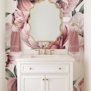 May include: A white bathroom vanity with gold fixtures and a scalloped mirror. The wall is decorated with a large floral mural in pink and mauve tones. Two pink towels hang on gold towel rings.