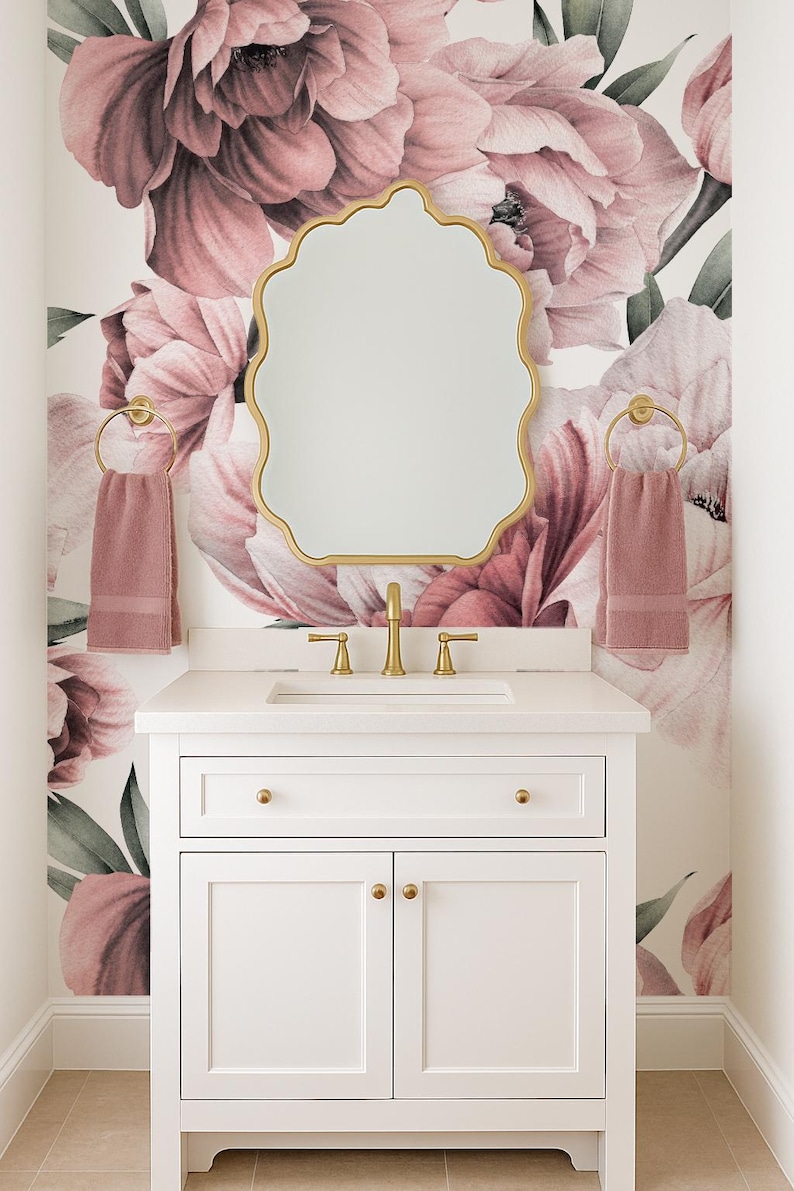 May include: A white bathroom vanity with gold fixtures and a scalloped mirror. The wall is decorated with a large floral mural in pink and mauve tones. Two pink towels hang on gold towel rings.