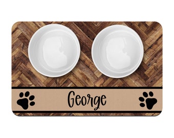 Pode incluir: Um tapete para tigelas de cachorro marrom e bege com um padrão de grão de madeira. O tapete tem duas tigelas de cerâmica branca e uma faixa marrom e bege com o nome "George" e duas pegadas pretas.