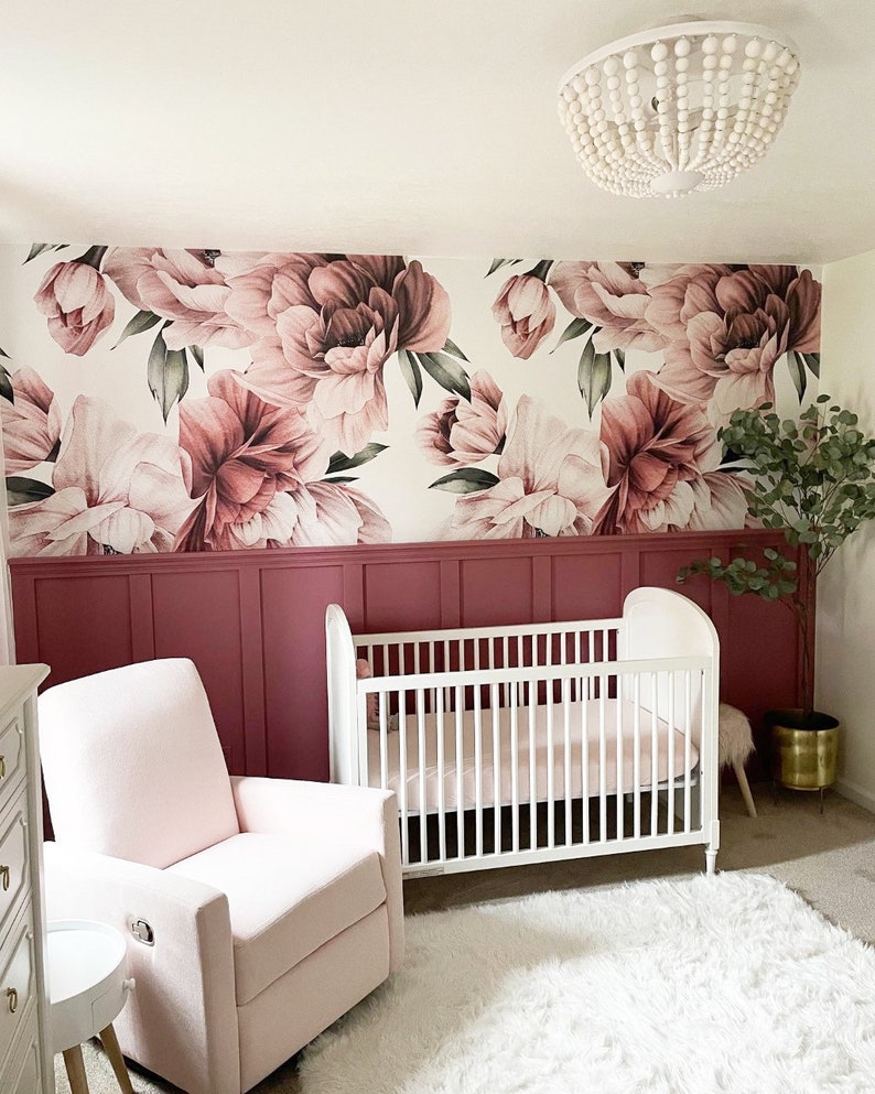 May include: A nursery decorated with floral wallpaper featuring large pink and mauve peonies. The room includes a white cot, a pink rocking chair, and a fluffy white rug. A decorative beaded chandelier hangs from the ceiling.