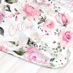 May include: White blanket with a watercolor floral design featuring pink roses and other flowers. The word "Collins" is written in pink script across the blanket. Green leaves and accents complete the design.
