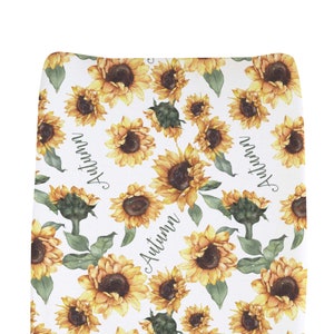 May include: White changing pad cover with a sunflower pattern and the name "Autumn" written in cursive.