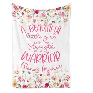 May include: A white floral blanket with the text "A beautiful little girl with the strength of a warrior" in pink lettering. The names "Elena Marie" are also written in pink lettering.