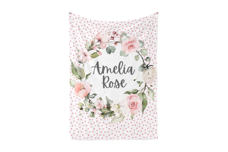 Puede incluir: Una manta de beb&eacute; blanca con un estampado de lunares rosas. El centro presenta una corona floral con el nombre "Amelia Rose" en escritura cursiva. La corona incluye rosas rosas, vegetaci&oacute;n y otras flores.
