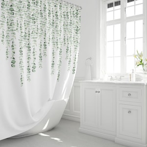 May include: White shower curtain with a green eucalyptus leaf pattern. The leaves are hanging down from the top of the curtain.
