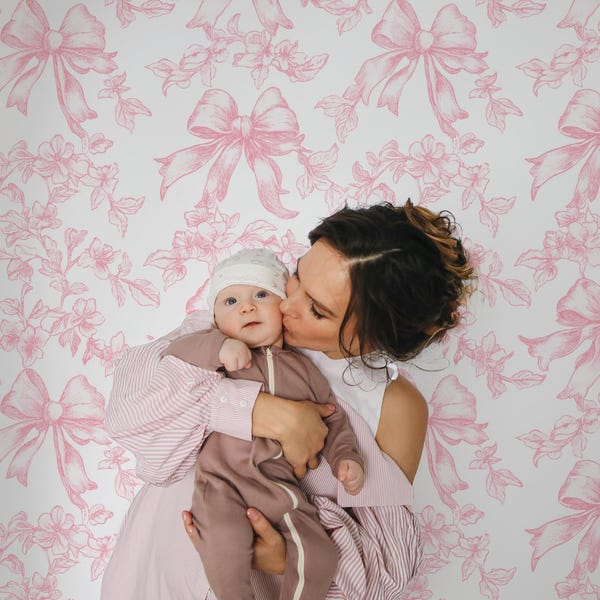 May include: Wallpaper featuring a repeating pattern of pink bows and floral sprigs on a white background. The design consists of hand-drawn style illustrations of tied ribbons and delicate blossoms arranged in a consistent, decorative layout.