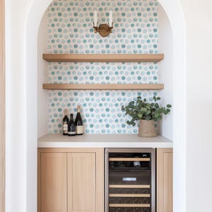 May include: A built-in arched bar nook featuring light wood cabinetry, a stainless steel wine refrigerator, and two floating shelves. The back wall is covered in white wallpaper with a pattern of teal and light blue watercolor-style polka dots.