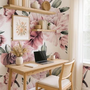 May include: A home office setup featuring a wooden desk, chair, and shelves. A laptop, notebook, and mug are on the desk. The wall is adorned with a floral mural of pink and purple blooms. A framed floral print and vase with dried flowers are also visible.