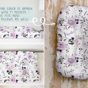 May include: A white changing pad cover featuring a floral pattern of purple roses, dark purple accents, and green leaves. The fabric includes the name Rosalie in script. Text states: CHANGING PAD COVER IS APPROX 32x16.5" WITH 7" POCKETS.