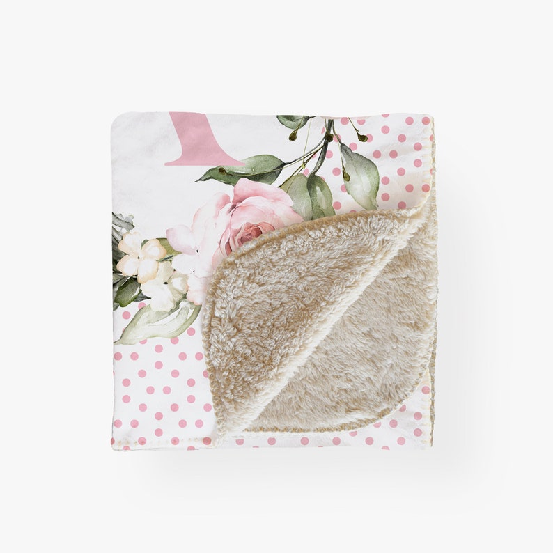 Puede incluir: Una manta blanca con un estampado de lunares rosas y un dise&ntilde;o floral. El dise&ntilde;o floral incluye rosas rosas, flores blancas y hojas verdes. La manta tiene un suave forro de sherpa beige.