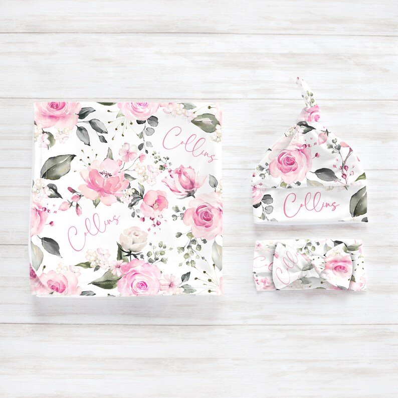 May include: A baby blanket, hat, and headband set. The items feature a floral pattern with pink roses, green leaves, and the name "Collins" in pink script. The set is designed for newborns.