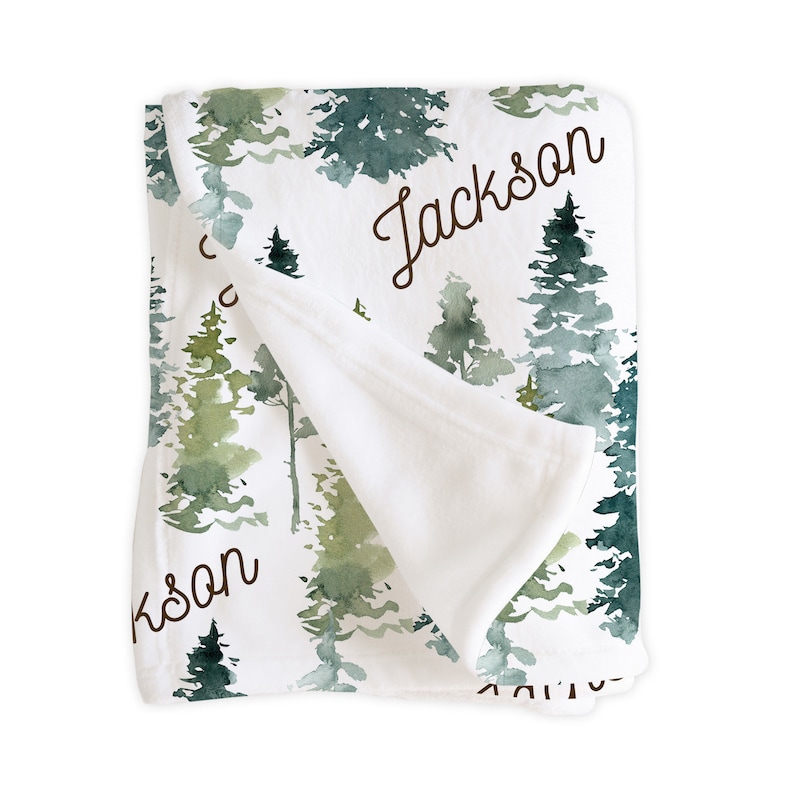 May include: A white baby blanket with a watercolor forest print and the name "Jackson" written in brown cursive.