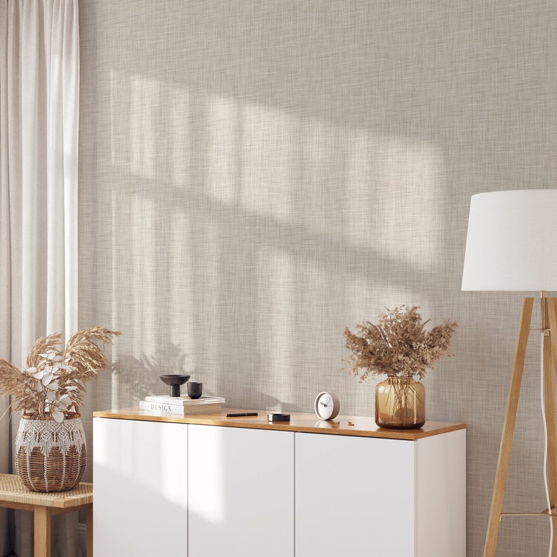 May include: White cabinet with two doors and a wood top. The cabinet is against a wall with a light beige textured wallpaper. A vase with dried flowers, a clock, and a book titled "Design" are on the top of the cabinet.