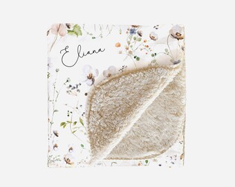 May include: A white and beige baby blanket with a floral pattern and the name "Eliana" written in cursive. The blanket is made of soft, plush fabric.