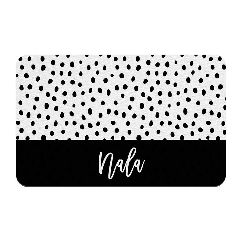 May include: Black and white doormat with a white background and black polka dots. The bottom half of the doormat is black with the name "Nala" written in white.