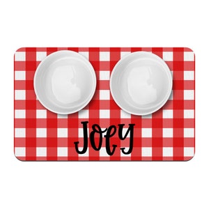 May include: Red and white checkered dog bowl mat with two white bowls and the name "Joey" printed in black.