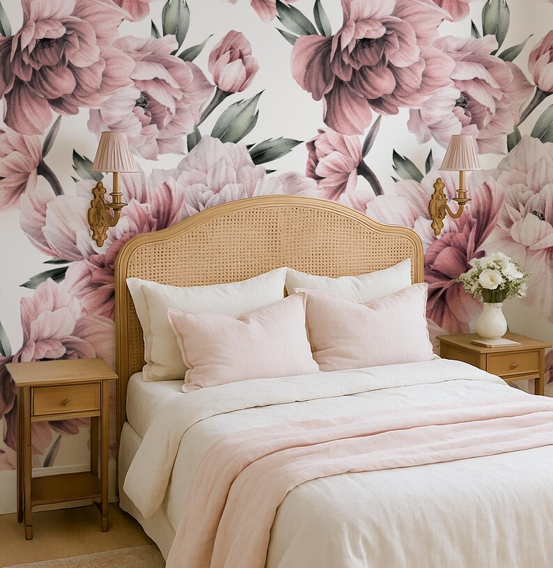 May include: A bedroom with a bed featuring a woven headboard, white bedding, and pink pillows and throw. The wall is decorated with a large floral wallpaper in pink and white. Two small wooden bedside tables are on either side of the bed.