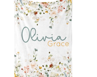 May include: A white baby blanket with a floral design in shades of pink, yellow, and green. The blanket has the name "Olivia Grace" written in blue and orange lettering.