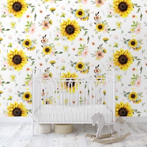 May include: A white metal crib stands before a wall covered in wallpaper featuring a repeating pattern of large yellow sunflowers, small pink flowers, and green foliage. A light-colored wooden rocking horse sits on the floor in front of the crib.