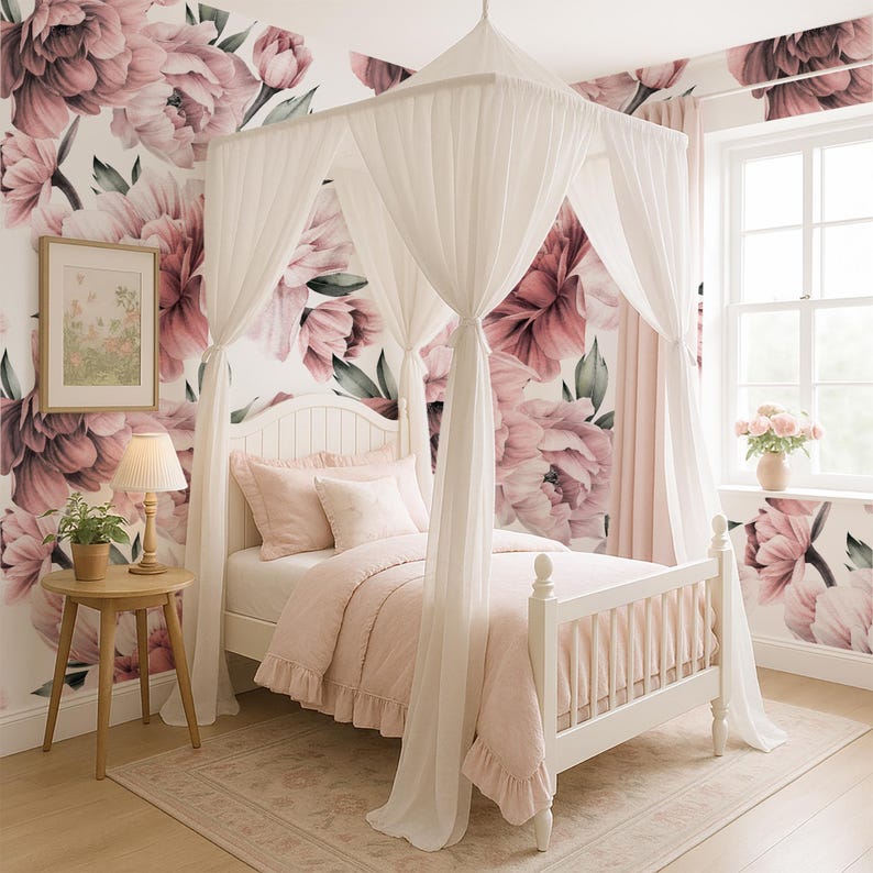 May include: A white canopy bed with pink bedding and pillows is set against a floral wallpaper backdrop. A small wooden side table with a lamp and a framed picture are next to the bed. The room has a soft, feminine aesthetic.