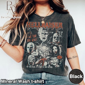 May include: A charcoal gray mineral wash t-shirt featuring a Hellraiser graphic print. The design includes multiple character portraits, the Lament Configuration puzzle box, and text reading "HELLRAISER," "HE'LL TEAR YOUR SOUL APART," "IT'S ME!," "YOU CAN GO TO HELL!," "OUCH, THAT REALLY HURTS," "STINKY," "GHEE," and "NO TEARS, PLEASE. IT'S A WASTE OF GOOD SUFFERING."