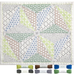 Könnte beinhalten: Weißes Textil mit geometrischem Design in braunen, grünen, blauen und weißen Stichen. Das Design zeigt Dreiecke und Sternmuster. Darunter befinden sich mehrere Garnrollen in verschiedenen Farben, darunter Grün, Braun, Blau und Grau.