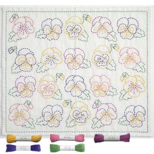May include: White embroidered cloth featuring a repeating pattern of pansies in pink, yellow, and purple thread. The pansies are outlined with a dashed stitch, and the leaves are green. Below are spools of embroidery thread in various colors.