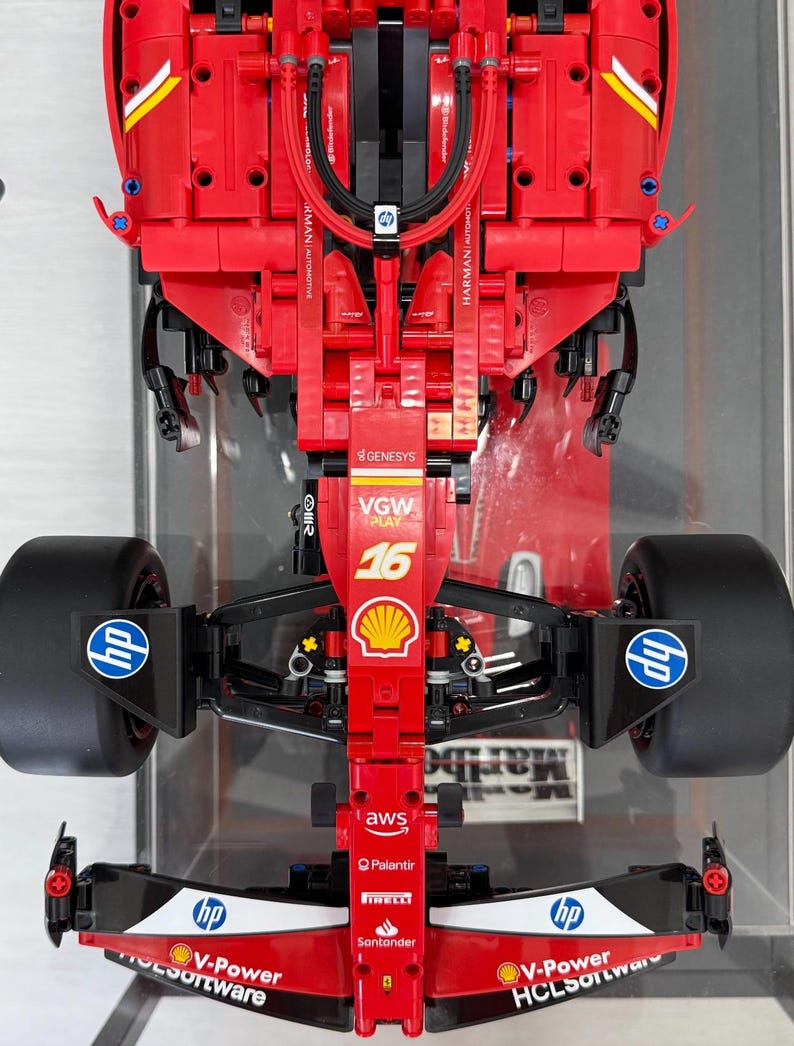 Pode incluir: Um modelo Lego vermelho e preto de um carro de corrida de F&oacute;rmula 1 com o n&uacute;mero 16 no lado. O carro tem patrocinadores como Shell, V-Power e Genesys. O carro est&aacute; em um expositor.