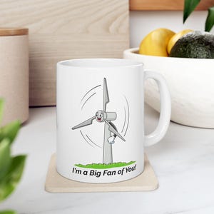 May include: White ceramic mug featuring a cartoon wind turbine with a smiling face. The mug has the text "I'm a Big Fan of You!" printed on the bottom.