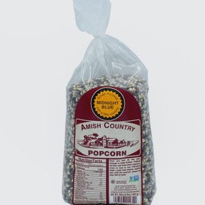 May include: A clear plastic bag filled with Midnight Blue Amish Country popcorn. The bag has a maroon label with the words "Amish Country Popcorn" and a graphic of a farm. The bag contains 2 lbs (907 g) of popcorn.