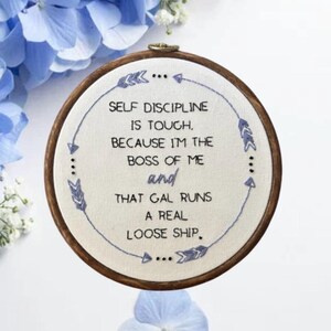 May include: Embroidered hoop art with the text "SELF DISCIPLINE IS TOUGH, BECAUSE I'M THE BOSS OF ME and THAT GAL RUNS A REAL LOOSE SHIP." The design features blue stitching and decorative arrows, set against a white fabric, with a wooden hoop.