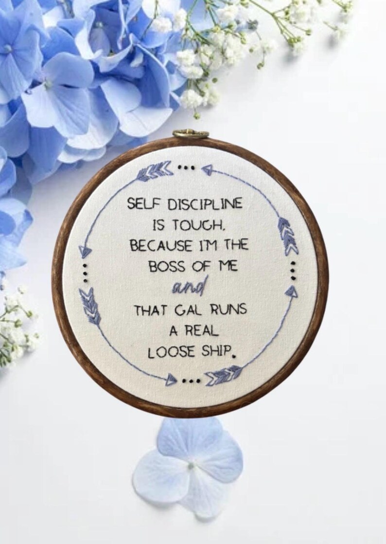 May include: Embroidered hoop art with the text "SELF DISCIPLINE IS TOUGH, BECAUSE I'M THE BOSS OF ME and THAT GAL RUNS A REAL LOOSE SHIP." The design features blue stitching and decorative arrows, set against a white fabric, with a wooden hoop.