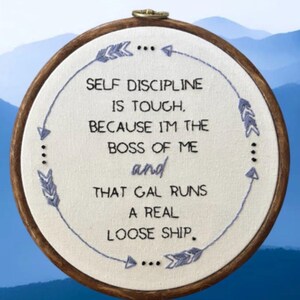 May include: Embroidered hoop art with the text "SELF DISCIPLINE IS TOUGH, BECAUSE I'M THE BOSS OF ME and THAT GAL RUNS A REAL LOOSE SHIP." The text is in black, with blue arrow and dot accents. The hoop is brown.
