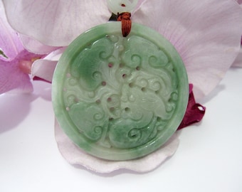 Op de afbeelding: Een groene jade hanger met ingewikkelde gravures van een bloemenmotief. De hanger is rond en heeft een gat aan de bovenkant voor een koord of ketting.