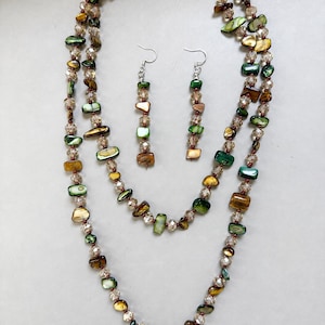 May include: A long necklace and a pair of matching drop earrings featuring a strand of iridescent green and brown shell beads interspersed with clear, faceted crystal beads. The earrings consist of a single vertical line of these beads.